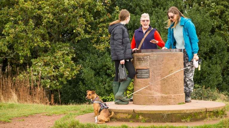 A family of visitors with their dog standing around the Toposcope, a cylindrical stone table, at Clent Hills